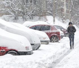 Mujer andando por una calle completamente nevada con coches