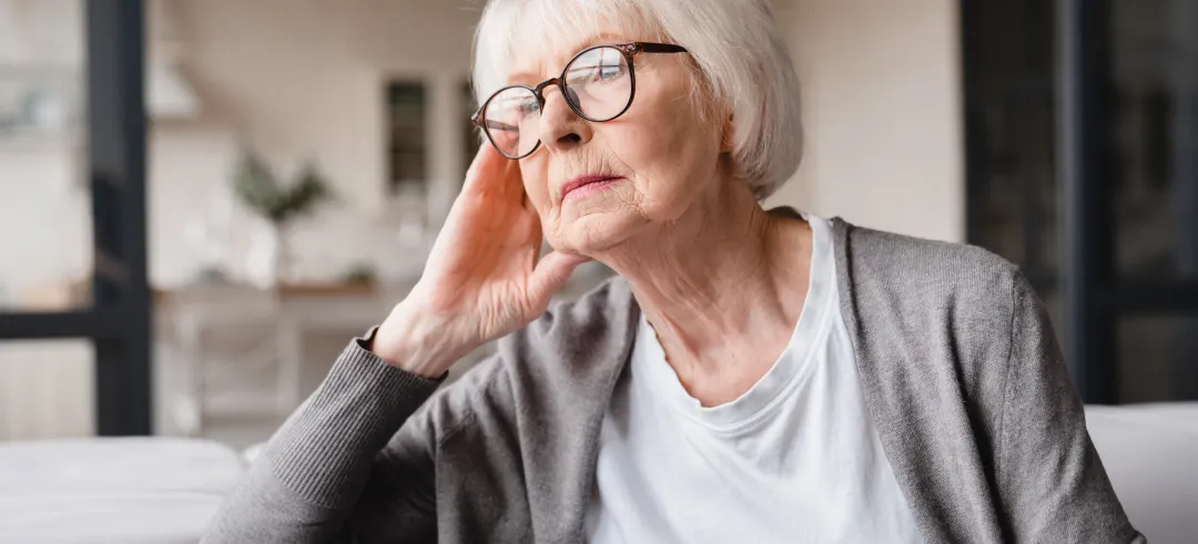 Mujer mayor pensativa, sentada en el sofá y mirando por la ventana