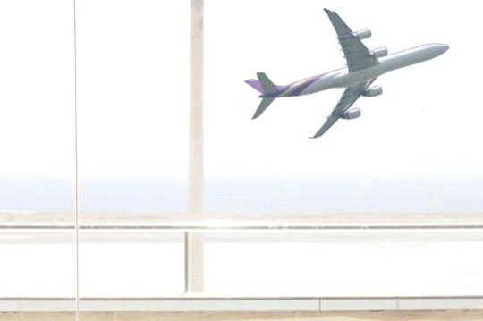 Mujer mirando por la ventana de un aeropuerto mientras despega un avión